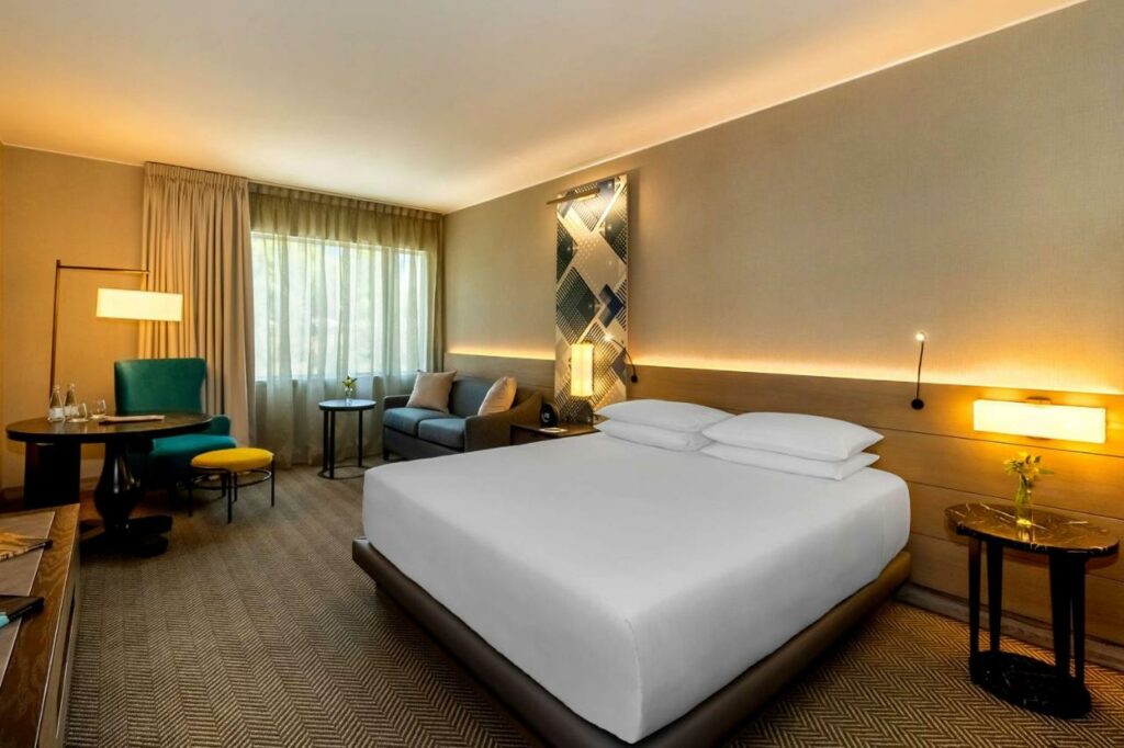 Quarto espaçoso no Hyatt Centric San Isidro Lima, com iluminação intimista e amarelada, cama de casal ampla e poltronas ao fundo