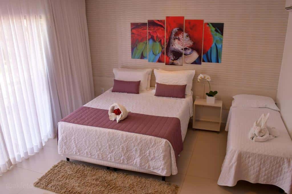 Uma cama bem arrumada com detalhes em roxo, uma mesa de cabeceira branca e arte na parede acima, ao lado de uma cama de solteiro com arte em toalha.