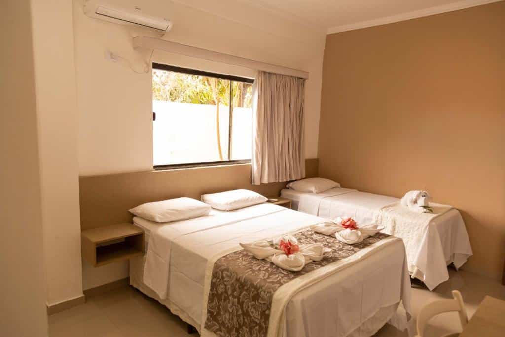 Um quarto de hotel com uma cama de casal e uma cama de solteiro, ambas bem arrumadas, com toalhas dobradas em cada cama.