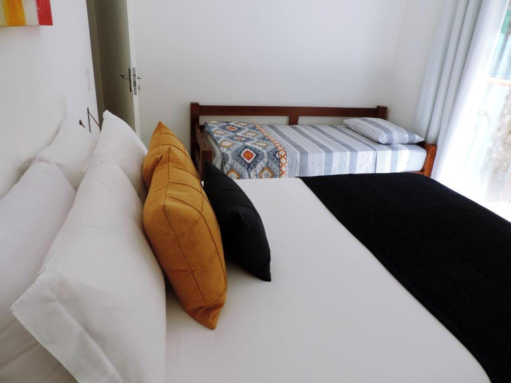 Uma cama bem arrumada com lençóis brancos e travesseiros amarelos e pretos ao lado de uma cama de solteiro com roupa de cama listrada em um quarto bem iluminado, no Estalagem Aconchego, para representar airbnb em Cunha.