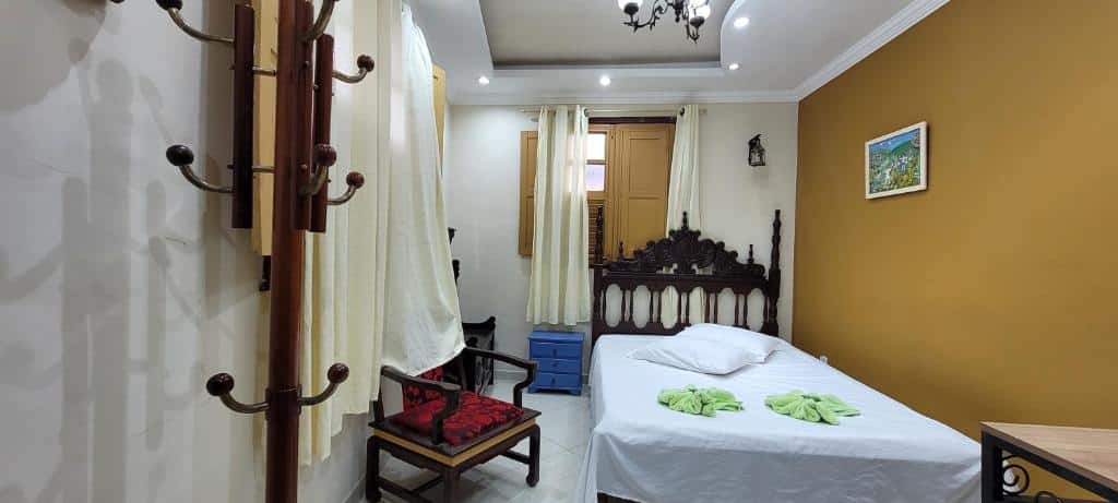 Foto do quarto do Apartamento completo no Centro histórico. Ilustra o post sobre airbnb em Ouro Preto. Há uma cama de casal mais à direita do quarto, e do lado esquerdo dela há uma mesa de cabeceira e uma cadeira. Atrás dela há uma janela. O teto possui um lustre.