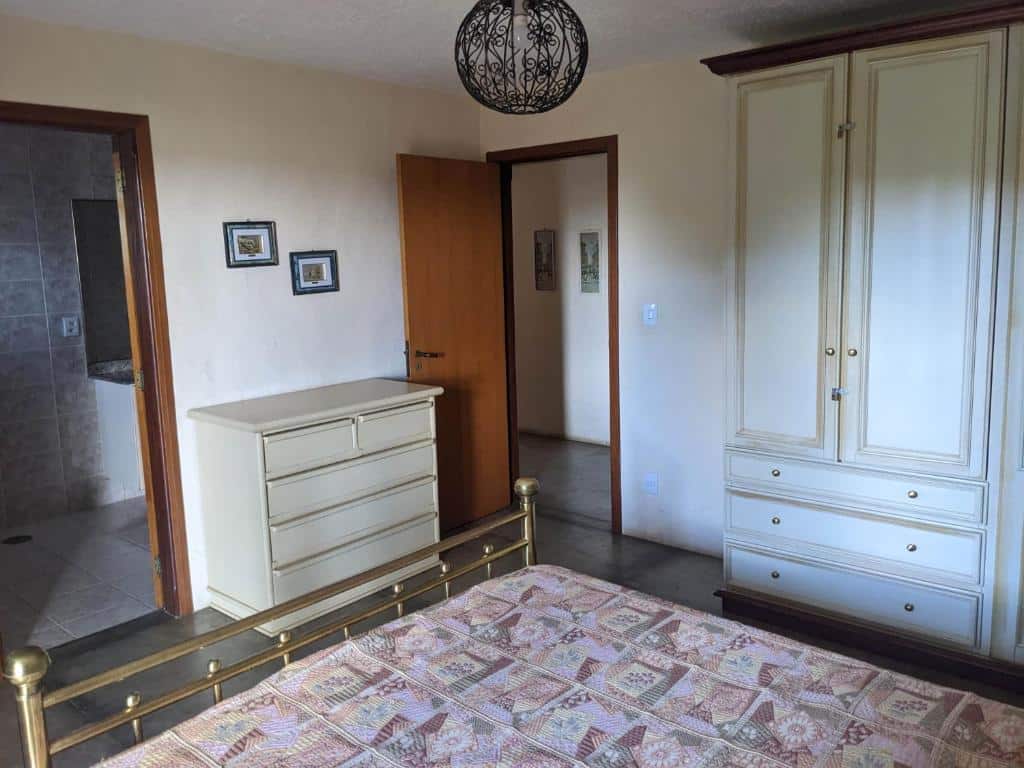 Foto do quarto em Chácara Santa Terezinha. A cama está no meio, vemos ela como quem está sentado. O guarda-roupa está ao lado direito, e também a porta do quarto. De frente há uma cômoda e porta para o banheiro, mais à esquerda. Ilustra o post sobre airbnb em Serra Negra.
