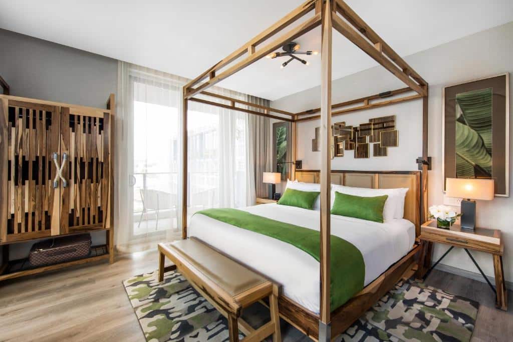 Quarto moderno do Lennox Miami Beach com cama de dossel, detalhes em verde, móveis de madeira, arte abstrata na parede e vista para a varanda.