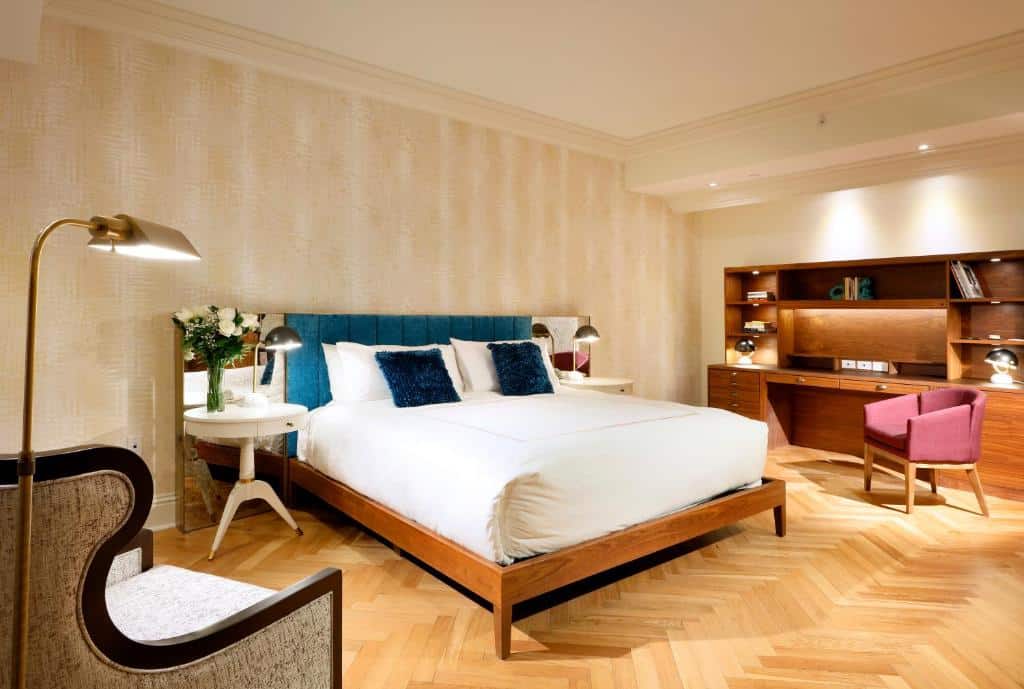 Quarto do Eurostars Langford com uma cama grande, piso de madeira, escrivaninha com cadeira, prateleiras de parede, duas mesas laterais e uma luminária decorativa. Representa hotéis em Miami.