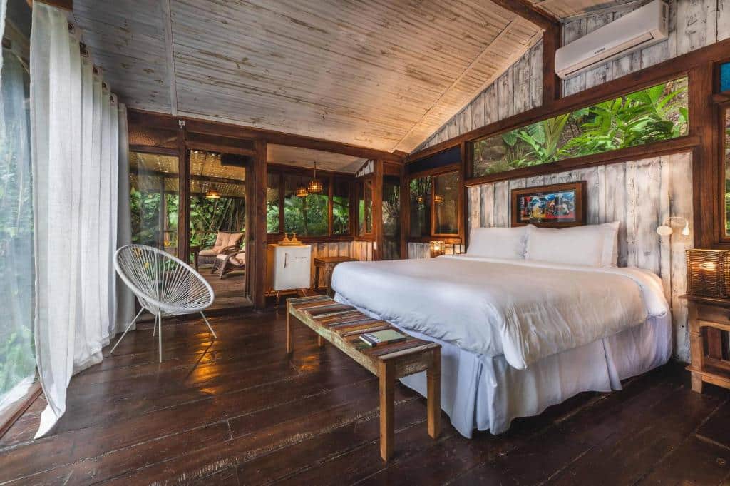 Quarto rústico na Casa Luz com tudo em madeira, uma cama de casal ampla, uma sacada grande, dois ambientes, cercado pelo verde da natureza, para representar hotéis em Paraty.