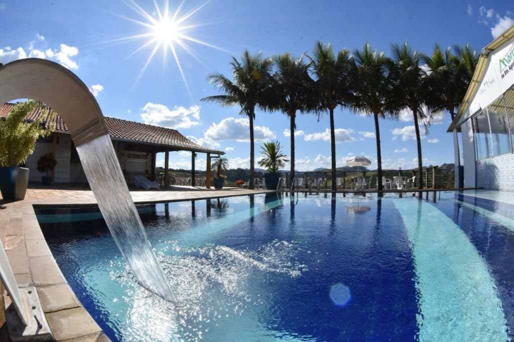 Piscina ampla e com uma pequena cascata no Hotel Morro De Santo Agostinho com palmeiras ao redor do deck