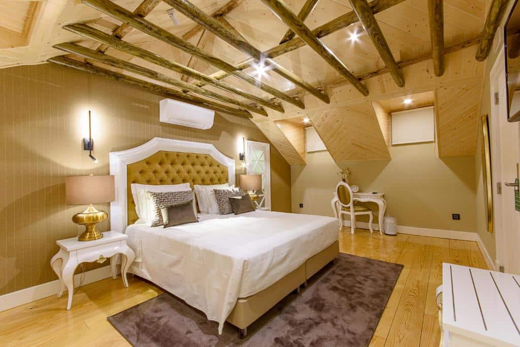 Um quarto com uma cama de casal, cabeceira dourada, vigas de madeira no teto, luminárias e uma escrivaninha com uma cadeira, na Villa Mariazinha Charming Hotel em Portimão.