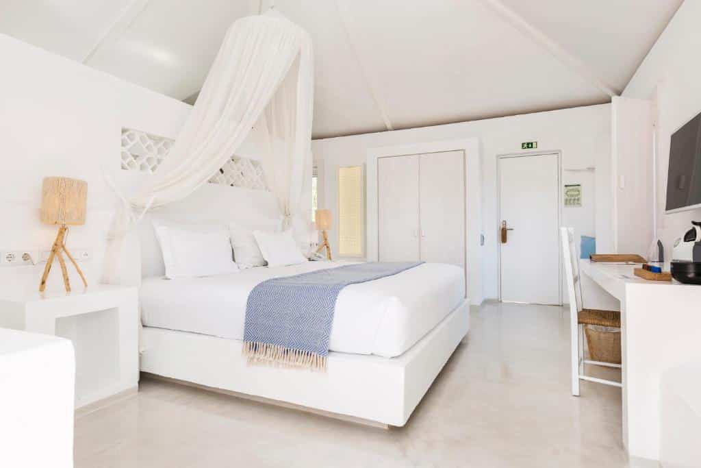 Quarto branco com uma cama de casal, cobertor azul, escrivaninha, cadeira, luminárias e uma porta com uma placa de saída acima dela, na Vila Monte Farm House em Moncarapacho, para representar hotéis em Algarve.