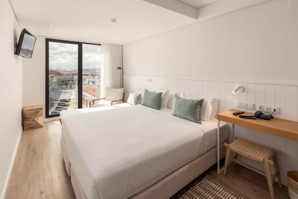 Um quarto moderno no Pure Formosa Concept Hotel em Olhão, com uma cama grande, escrivaninha, TV de tela plana, cadeira e janela com vista para a cidade, para representar hotéis em Algarve.