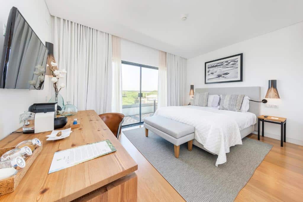 Um quarto moderno no Praia Verde Boutique Hotel na Praia Verde, com uma cama de casal, escrivaninha, TV, janela grande e decoração minimalista em tons neutros, para representar hotéis em Algarve.