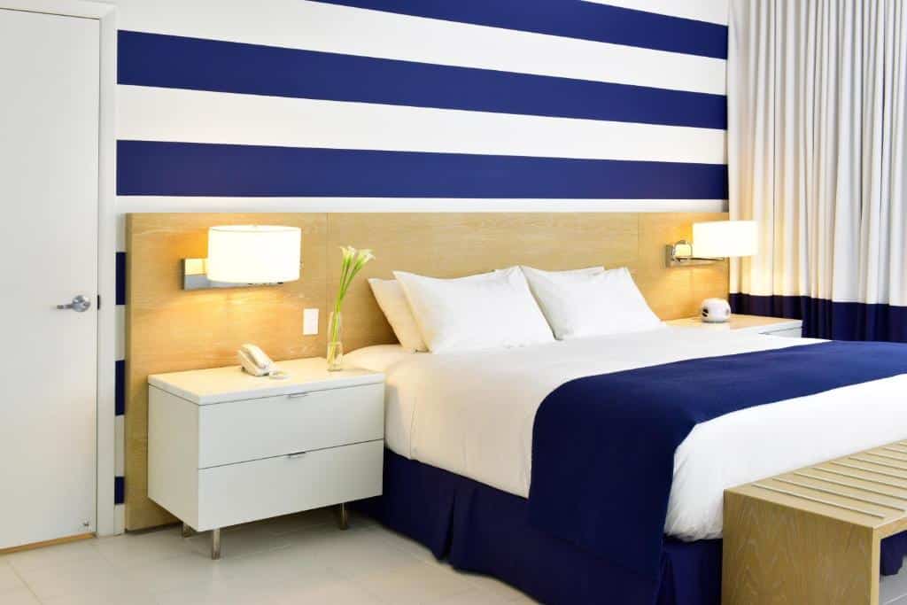 Quarto do Pestana South Beach Hotel com cama de casal do lado esquerdo da imagem com uma cômoda em cada lado da cama. Representa hotéis para Brasileiros em Miami.