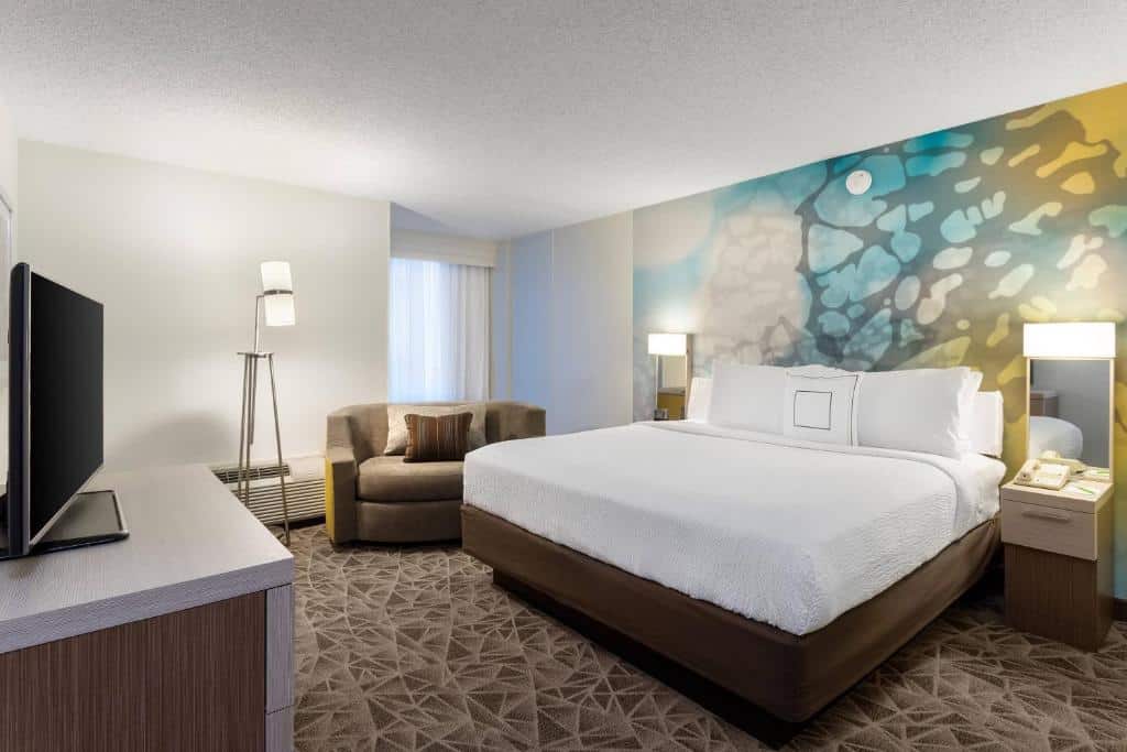 Quarto do Courtyard Miami Downtown Brickell Area com cama de casal do lado direito da imagem uma cômoda em cada lado da cama do lado direto uma poltrona em frente a cama uma cômoda com TV. Representa hotéis para Brasileiros em Miami.