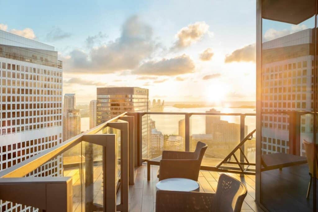 Imagem da varanda do EastMiami  durante o nascer do dia com a varanda do lado direito da imagem com duas cadeiras com vista para outros edifícios. 