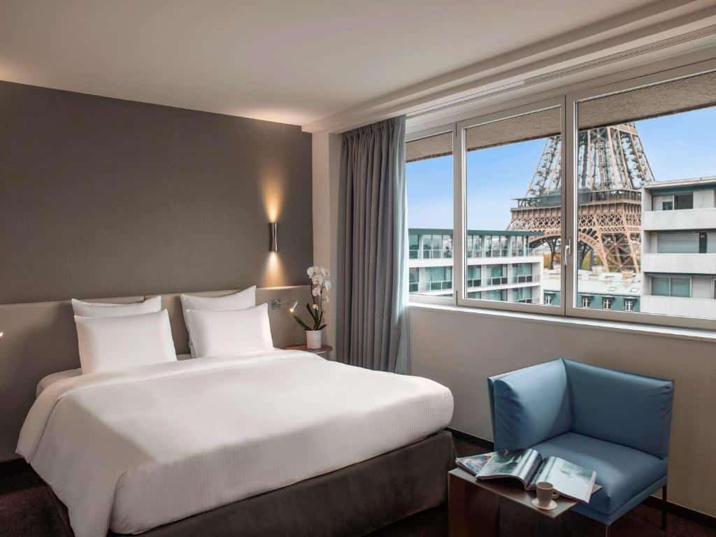 Quarto do Pullman Paris Tour Eiffel, um dos hotéis para família em Paris, com uma cama de casal, poltrona e janela grande com vista para a Torre Eiffel do lado de fora.