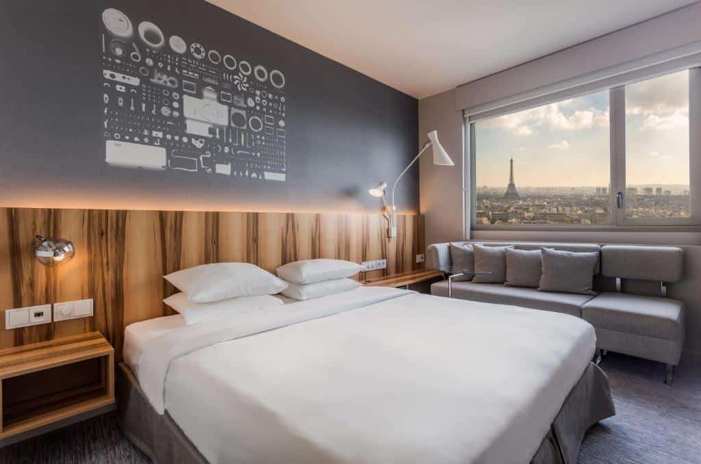 Quarto do Hyatt Regency Paris Etoile, sendo ele moderno com cama de casal, sofá, arte na parede e vista da Torre Eiffel e do horizonte de Paris pela janela.