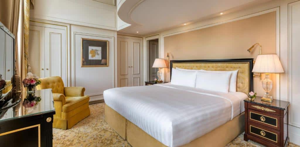 Quarto do Shangri-La Paris, um dos hotéis para família em Paris, sendo ele de luxo com uma cama grande, poltrona amarela, luminárias, arte na parede e decoração elegante em tons neutros.