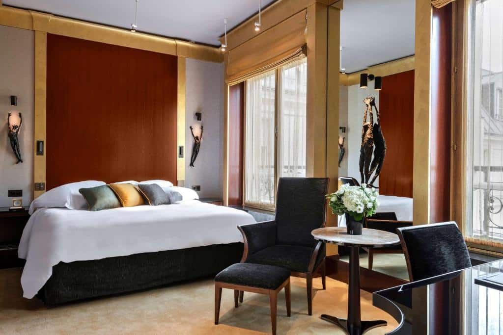 Quarto do Park Hyatt Paris Vendome, um dos hotéis para família em Paris, sendo ele moderno com uma cama de casal, travesseiros de realce, duas cadeiras, uma pequena mesa com flores e janelas grandes.