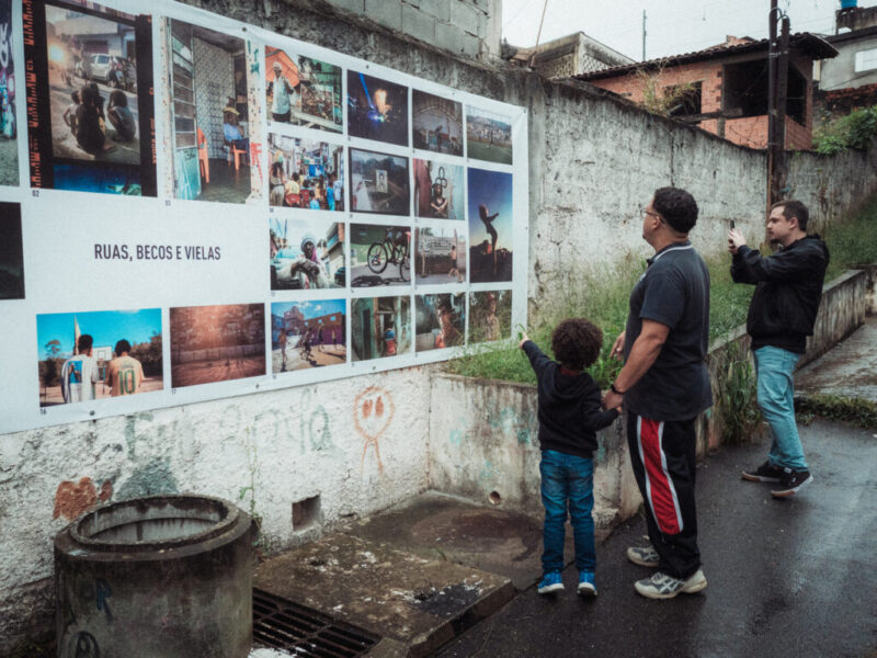 Pai e filho contemplam registros das periferias de São Paulo em Beco da Favela Monte Azul. Foto: Marlon Marinho/Uso autorizado.