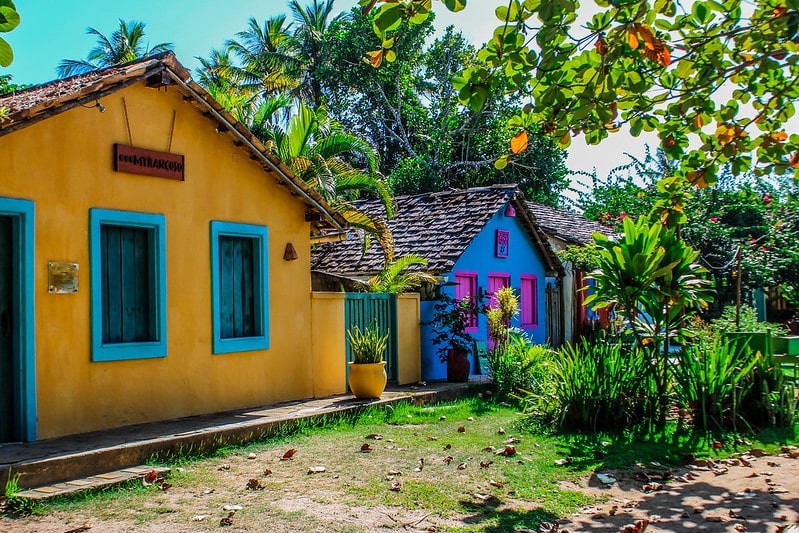 Foto de uma parte do Quadrado de Trancoso, mostrando um gramado verde com vários arbustos e plantas, além de ter uma casa amarela na esquerda e outra azul ao seu lado, mais para direita. 