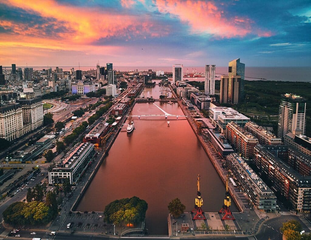 Entardecer cor de rosa refletindo na superfície do rio da Prata, que é cercado por prédios e outras construções.