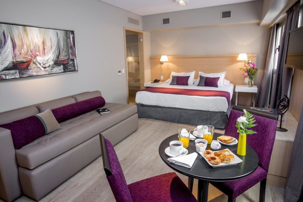 Quarto moderno no ARC Recoleta Boutique Hotel & Spa com uma cama de casal, sofá, mesa para o café da manhã e um quadro na parede, para representar onde ficar em Buenos Aires.