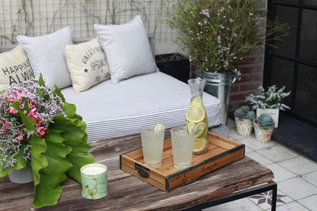 Uma mesa de madeira segura dois copos e uma jarra de limonada com limão; um sofá e plantas estão ao fundo, na propriedade da Casa Chic Palermo Soho.