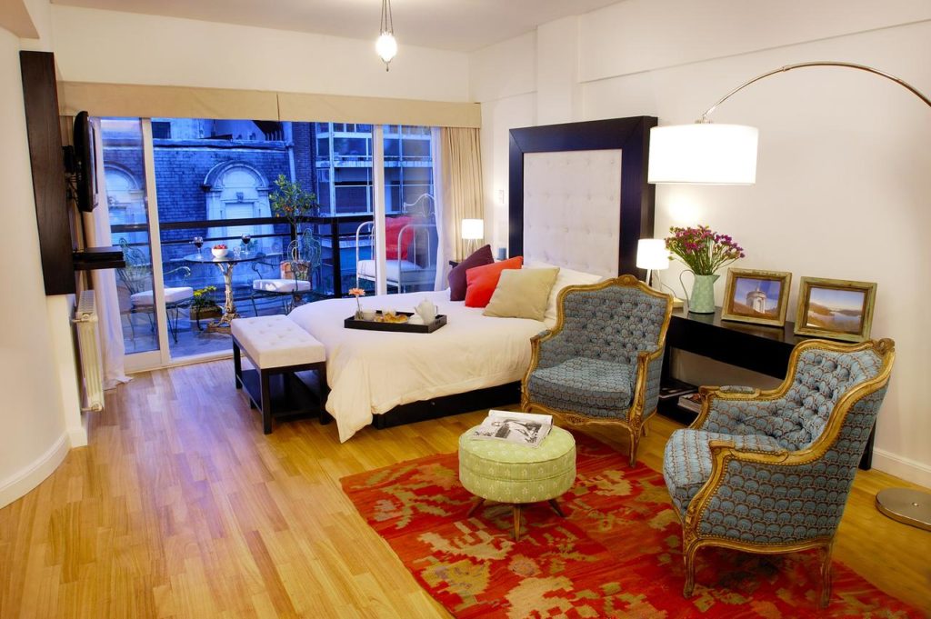 Um quarto com uma cama, duas poltronas estampadas, um tapete, uma luminária e uma varanda com assentos ao ar livre, no Poetry Building, para representar onde ficar em Buenos Aires.