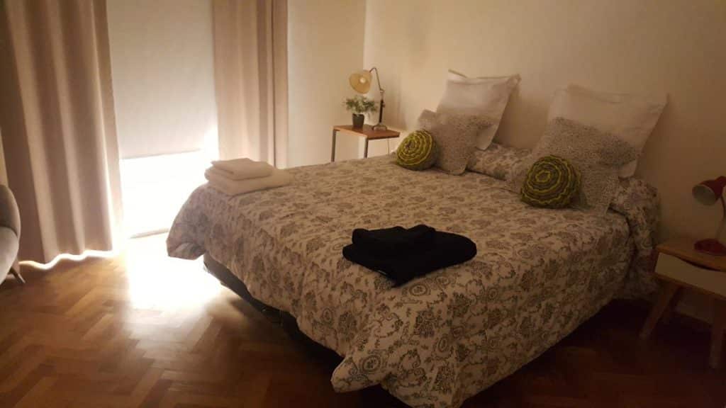 Uma cama de casal bem arrumada com roupas de cama estampadas, travesseiros e toalhas em um quarto suavemente iluminado com piso de madeira, no Las Heras Apartamento, para representar onde ficar em Buenos Aires.