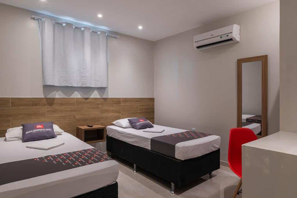 Um quarto com duas camas de solteiro, uma mesa de cabeceira, um espelho, uma cadeira vermelha e um ar-condicionado na parede, no Hotel Mega Aeroporto Fortaleza.
