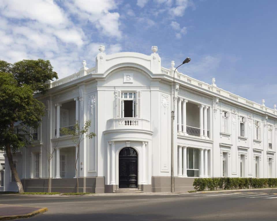 Frente do Hotel B, onde ficar em Lima. Um edifício neoclássico branco de dois andares com colunas decorativas e janelas grandes em uma esquina.