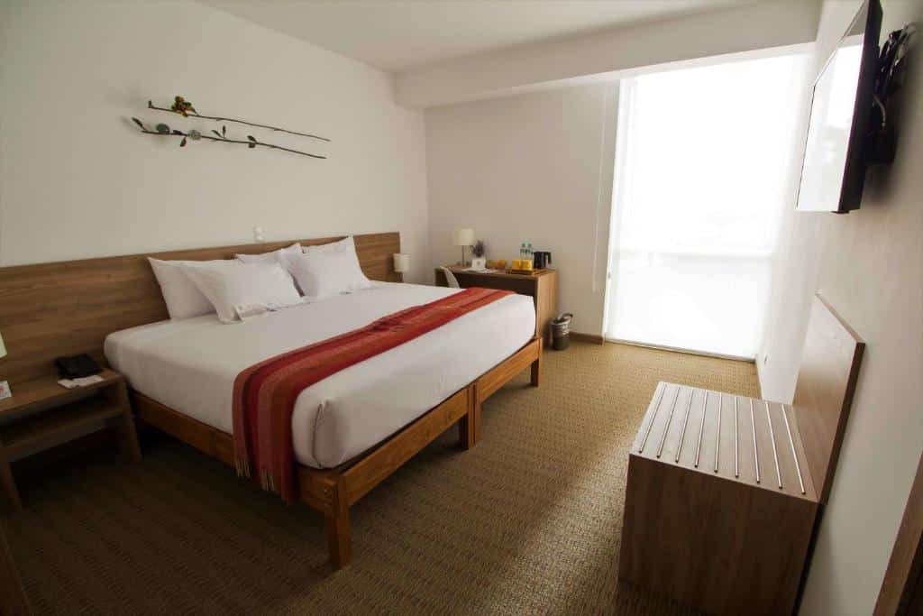 Quarto de um dos lugares onde ficar em Lima, o Tierra Viva. Um quarto de hotel com uma cama grande, escrivaninha, TV de tela plana e uma janela com cortinas transparentes que permitem a entrada de luz natural.