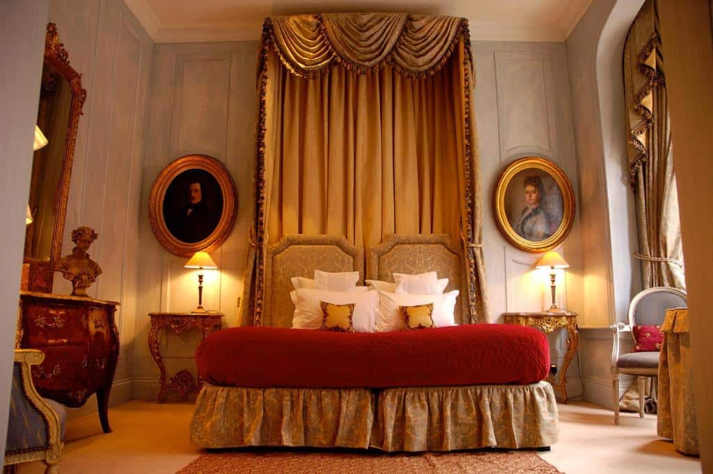 Quarto do San Domenico House com uma cama de casal e uma cabeceira com panos que chegam até o teto, duas mesinhas de cabeceira com abajures, quadros nas paredes, poltronas e uma janela com cortinas