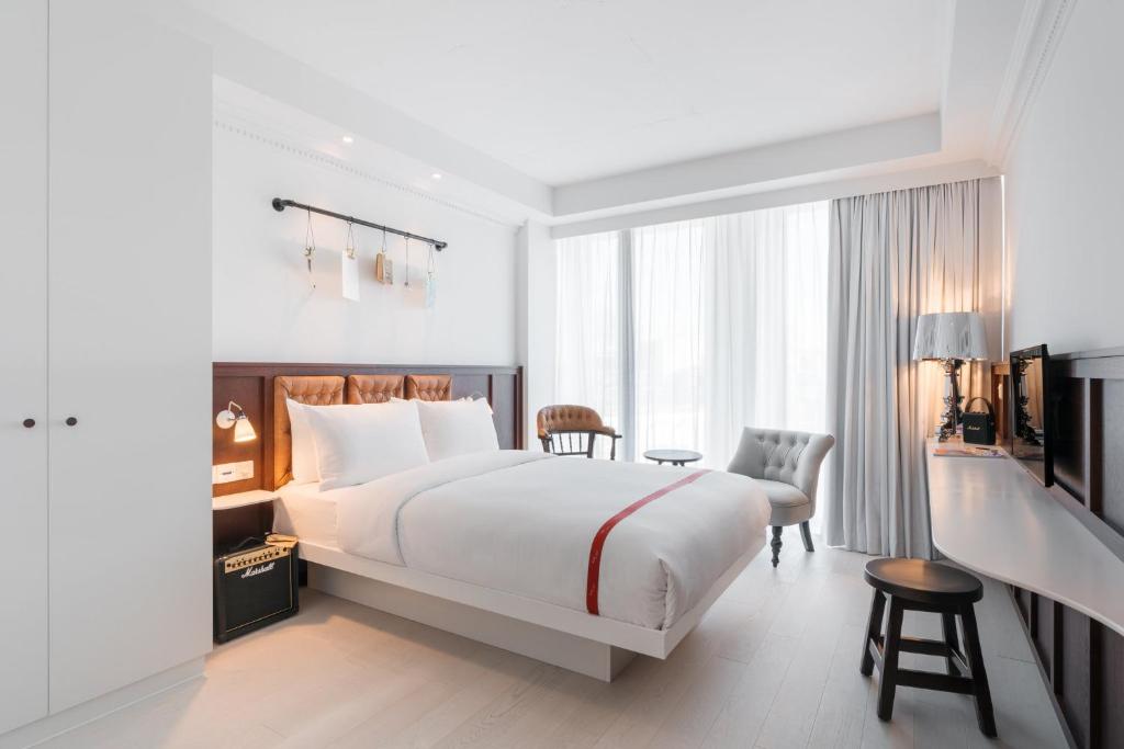 Quarto minimalista no Ruby Stella Hotel London com uma cama de casal, duas cadeiras, uma escrivaninha e janelas grandes com cortinas transparentes que deixam entrar a luz, para representar onde ficar em Londres.