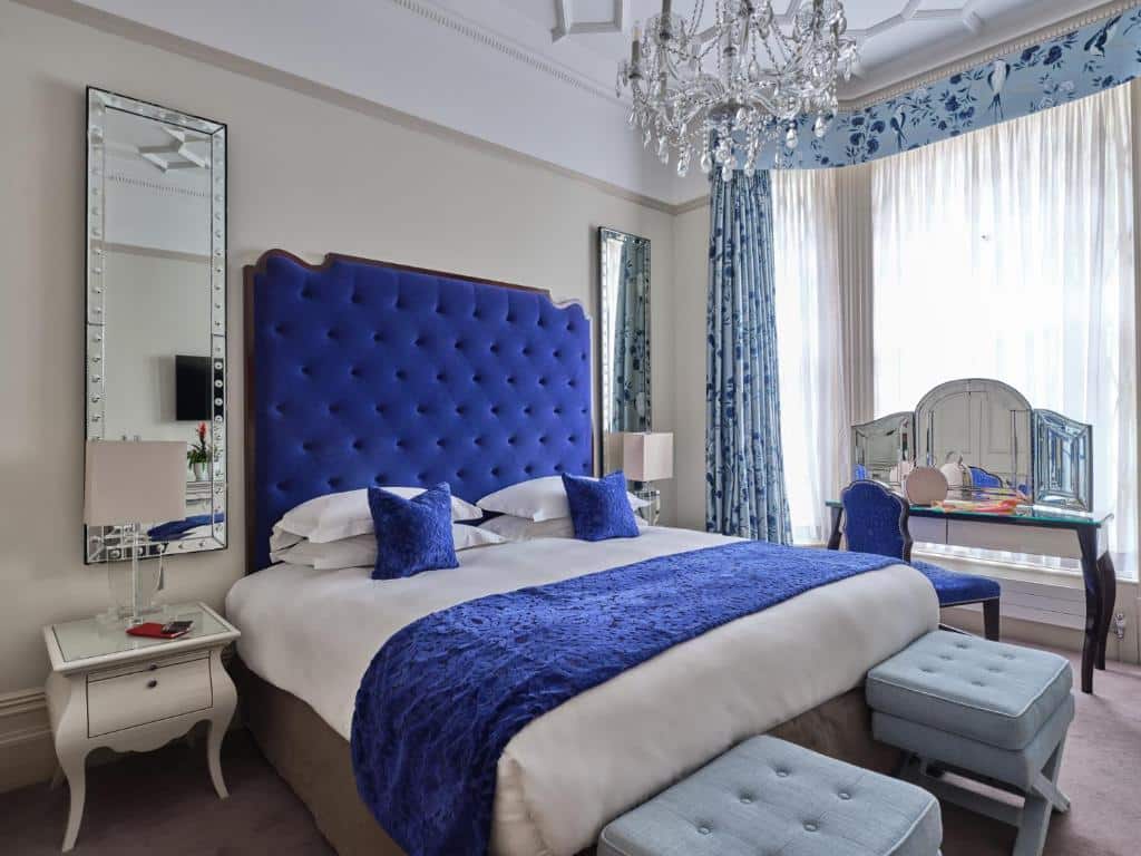 Quarto do The Apartments by The Sloane Club com uma cama de casal, dois espelhos, um lustre, uma jenal com cortinas, uma penteadeira, dois bufes e duas mesinhas de cabeceira.