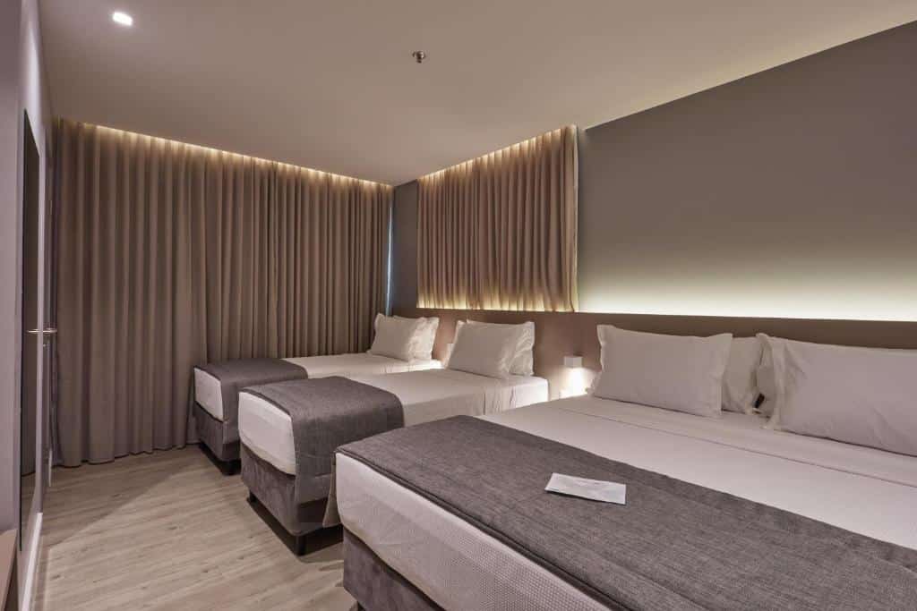 Um quarto no Flix Hotel na Praia de Jatiúca, com duas camas de casal, roupa de cama cinza, piso de madeira e cortinas cobrindo grandes janelas, para representar onde ficar em Maceió.