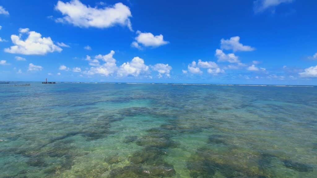 Mar raso e transparente, mostrando corais ao fundo, durante um dia ensolarado com poucas núvens, em Marco dos Corais em Maceió.