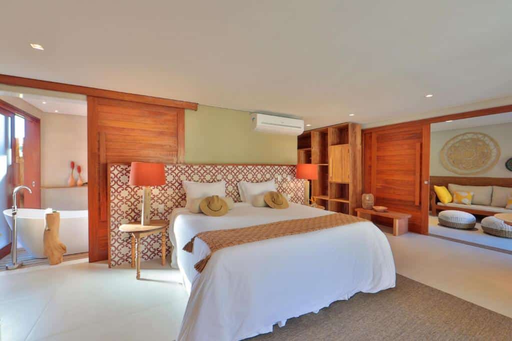Quarto de hotel espaçoso com uma cama king-size, cabeceira estampada, detalhes em madeira e uma área de estar com uma banheira próxima.
