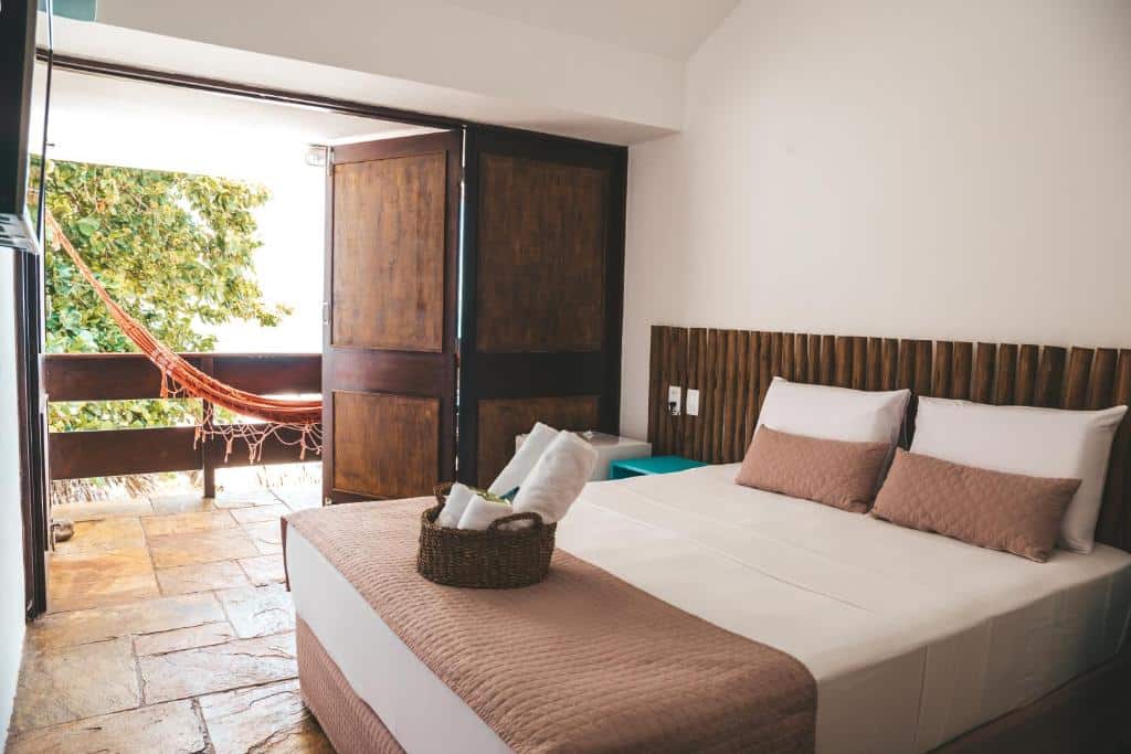 Um quarto simples com uma cama de casal, portas de madeira abertas e uma rede do lado de fora em uma varanda com azulejos de pedra. Esta é uma das opções onde ficar em Maragogi.