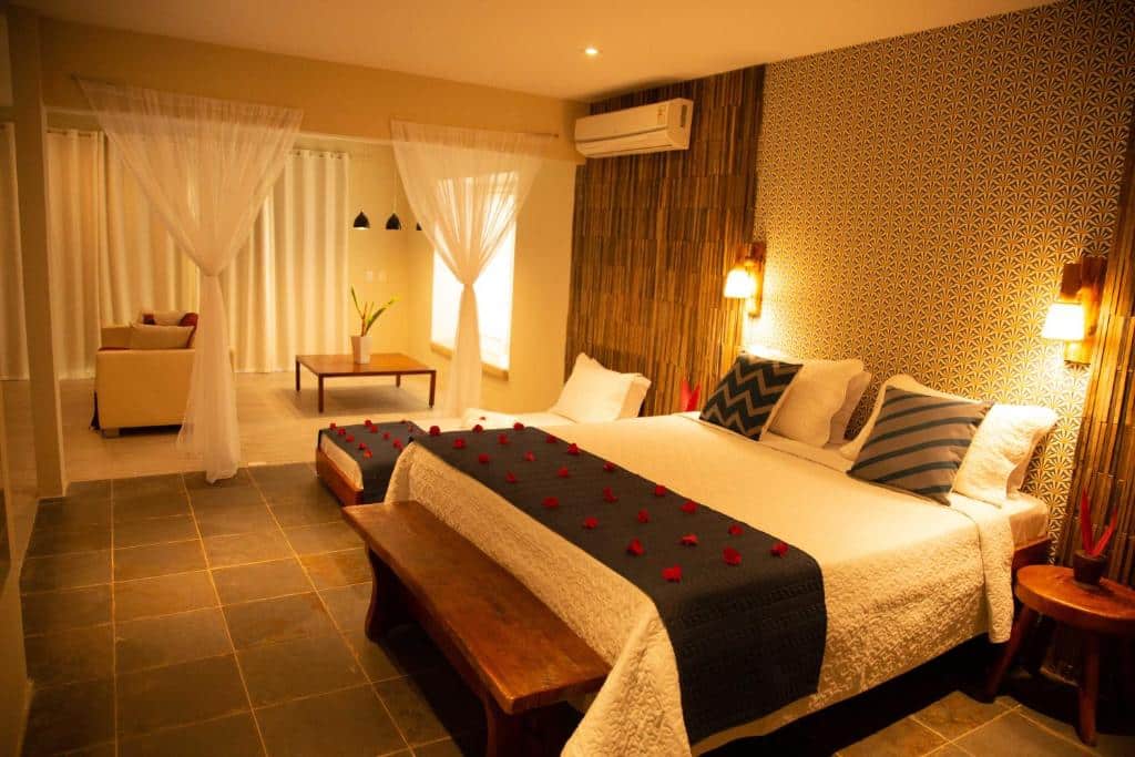 Um quarto de hotel com duas camas, parede estampada, bancos de madeira, área de estar e travesseiros e cobertores decorativos. Esta é uma das opções onde ficar em Maragogi.