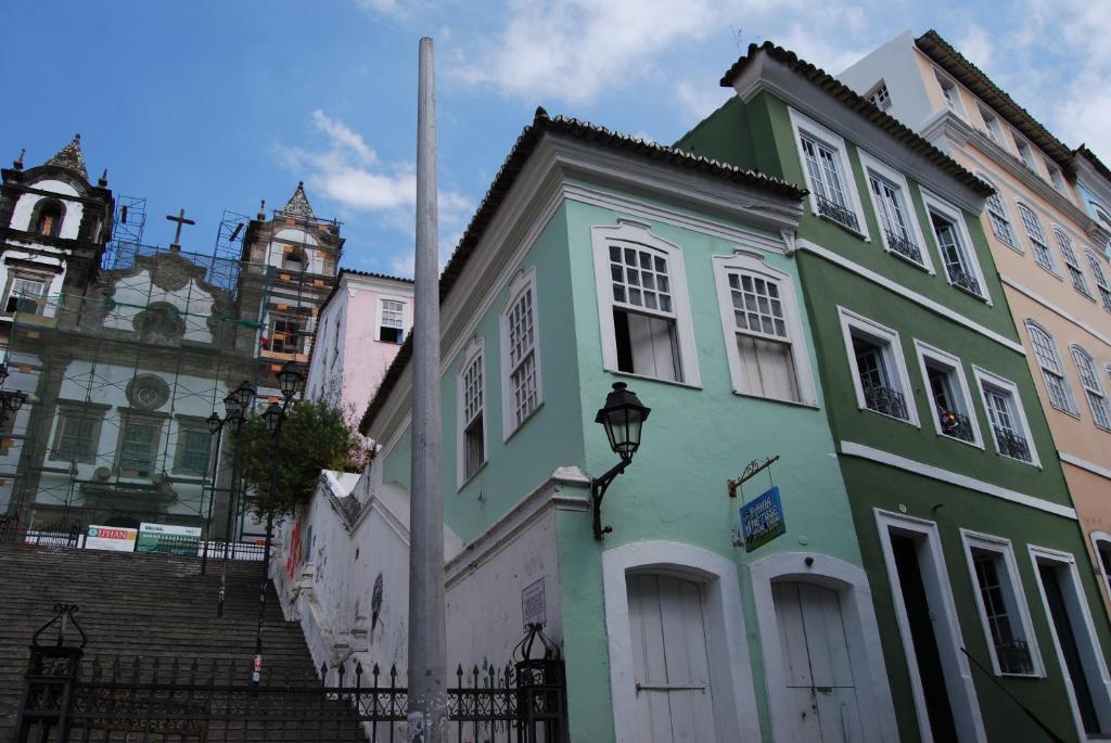 Um prédio verde em estilo colonial fica ao lado de uma escada que leva a uma igreja em reforma, com um céu azul acima.