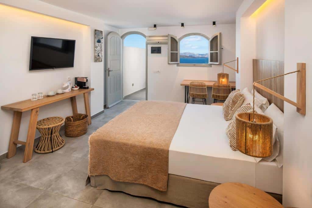 Quarto de hotel moderno com uma cama de casal, TV, escrivaninha, cestas e janelas abertas com vista para o exterior.