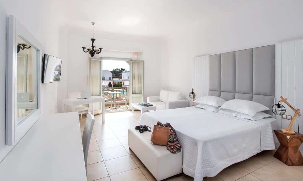 Quarto de hotel bem iluminado com uma cama de casal, sofá, TV, escrivaninha e portas de varanda abertas que permitem a entrada de luz natural.