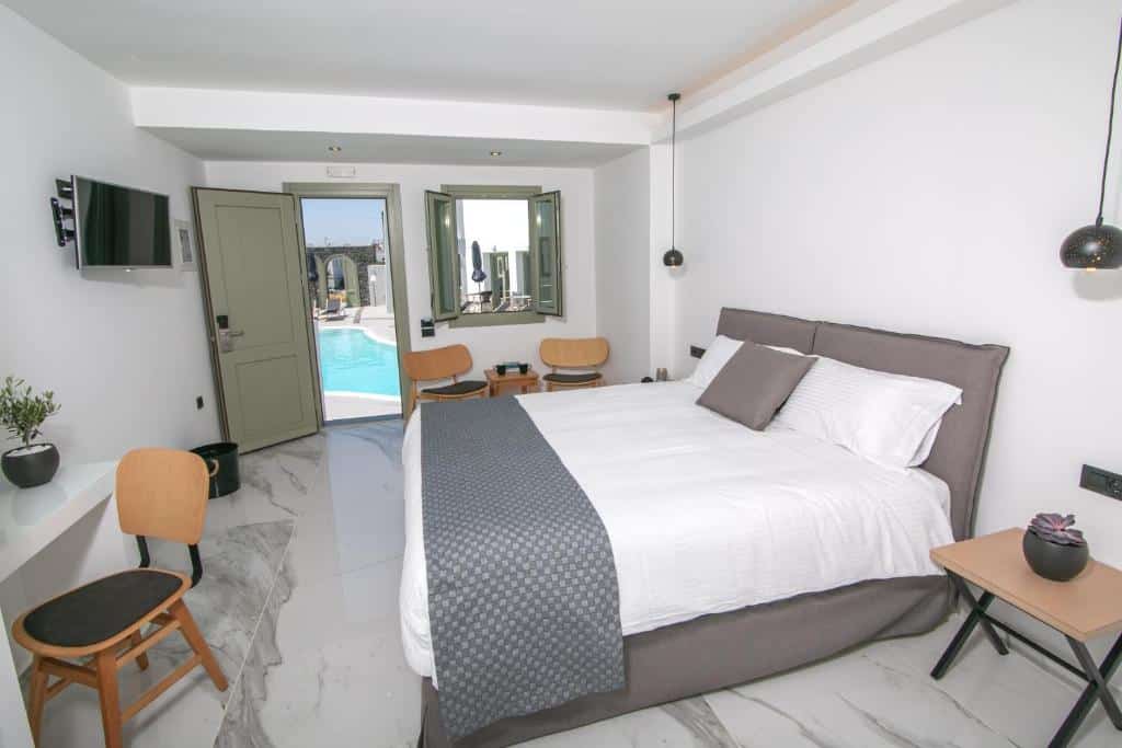 Quarto de hotel minimalista com uma cama de casal, cadeiras, TV e porta aberta que dá para a área externa da piscina.
