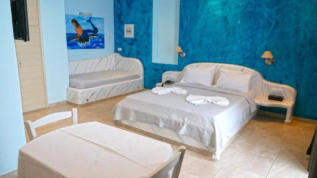 Quarto de hotel com uma cama de casal, sofá-cama de solteiro, mesa com cadeiras e paredes azuis texturizadas com uma pintura de golfinho.