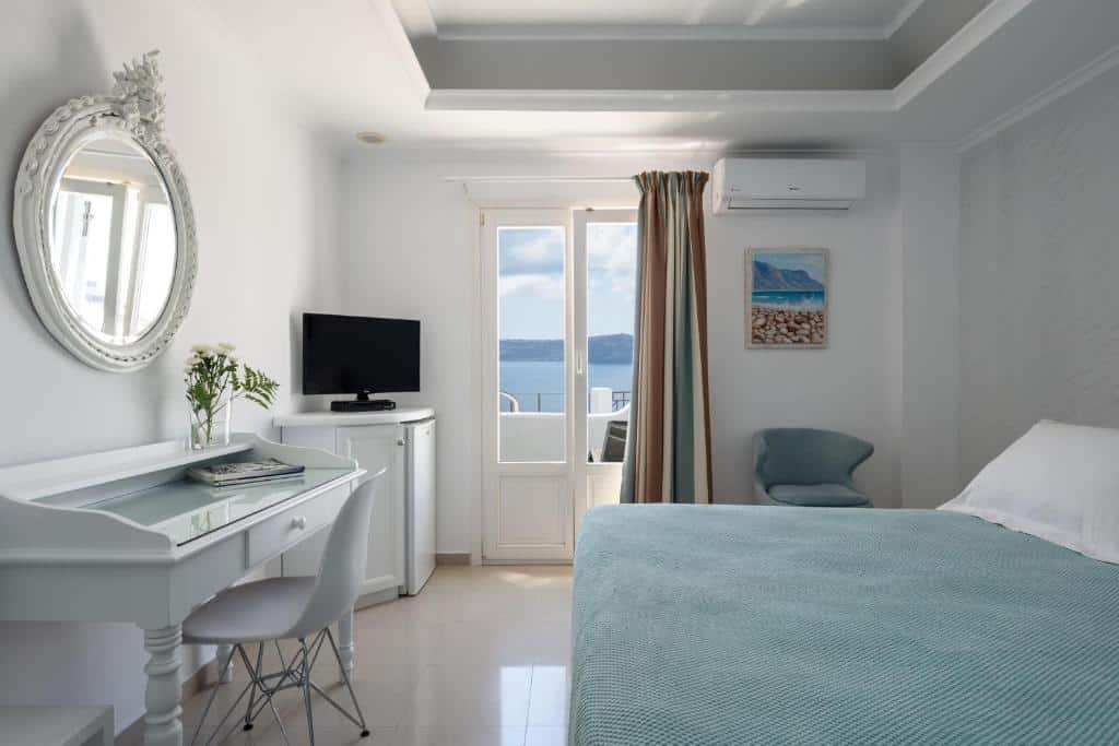 Um quarto branco bem arrumado com cama, escrivaninha, TV, frigobar e uma porta que dá para uma varanda com vista para o mar.