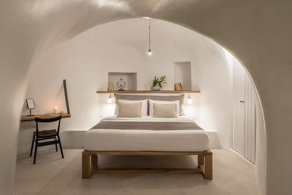 Quarto minimalista com uma cama grande, prateleiras embutidas, escrivaninha, cadeira, iluminação suave e paredes e teto brancos em arco.