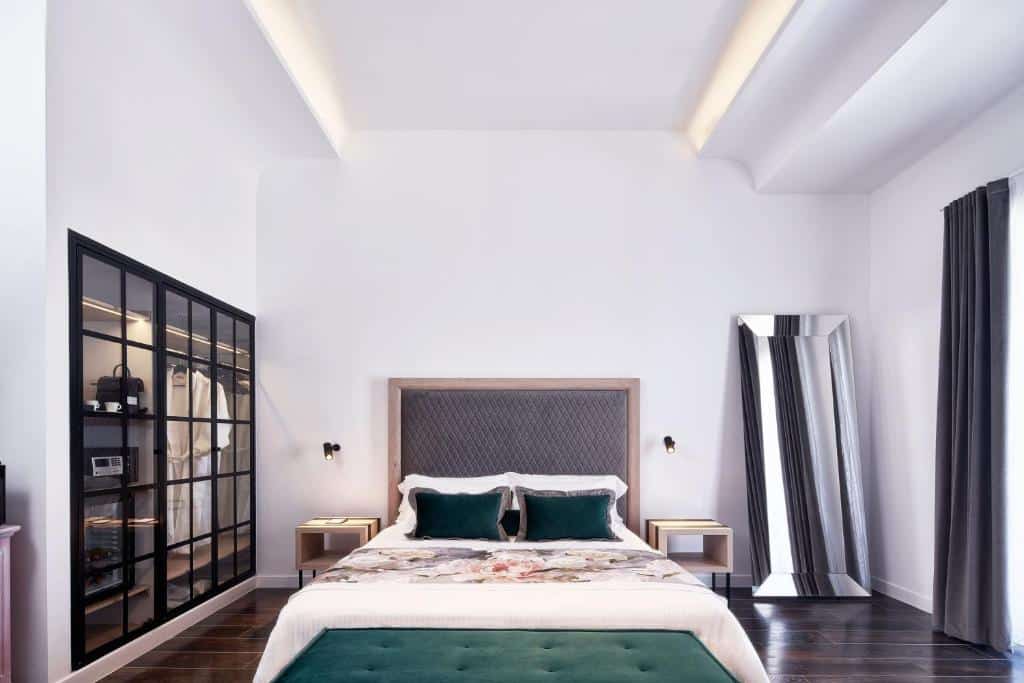 Um quarto moderno com uma cama de casal, cabeceira estofada, espelho no chão, guarda-roupa de vidro e piso de madeira escura.