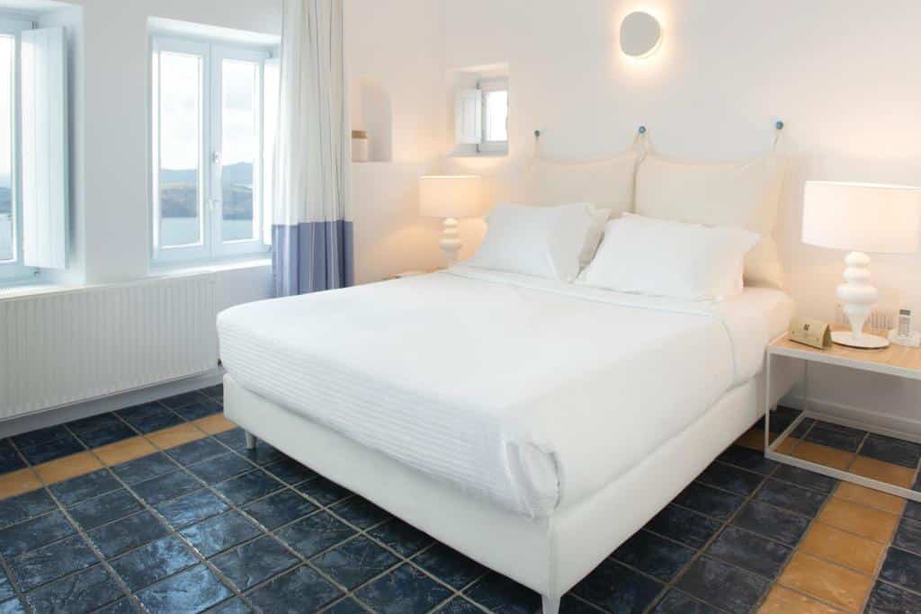 Quarto minimalista com paredes brancas, uma cama de casal, duas mesas de cabeceira com luminárias e piso de azulejos azuis.