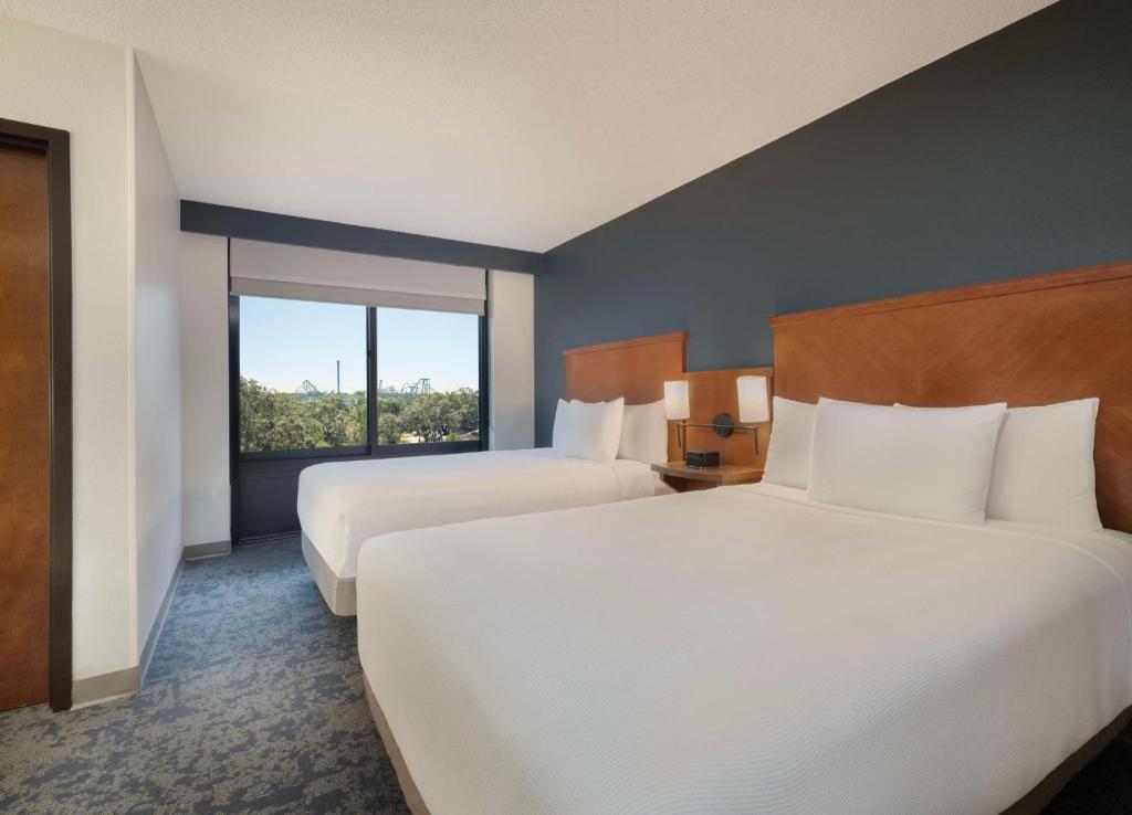 Quarto no Hyatt Place Tampa Busch Gardens com duas camas de casal, roupa de cama branca, parede escura com detalhes, janela com vista para o exterior e mesa de cabeceira com luminárias, para representar onde ficar em Tampa.