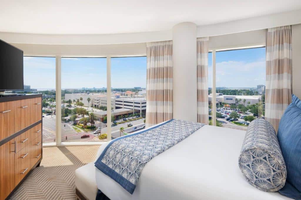 Quarto no The Westshore Grand com uma cama de casal com vista para duas janelas amplas, uma cômoda e uma televisão.
